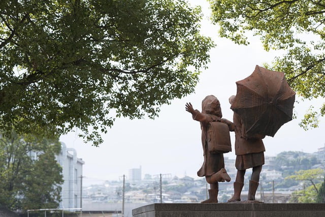 木々の中に設置された合羽を着た子どもと傘をさす子どもの彫像